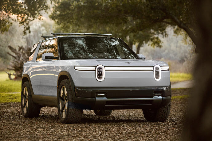 Front three-quarter view of a white Rivian R2 with illuminated headlights